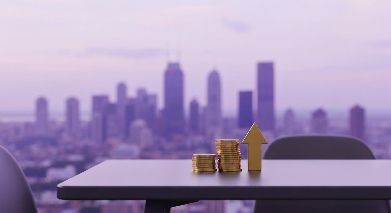 Stack of gold coins and upward arrow on a modern office table with a cityscape in the background
