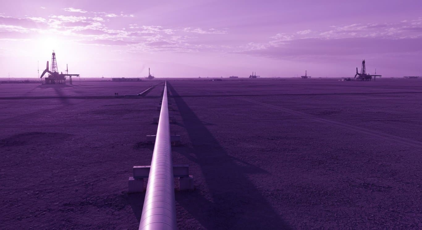 Natural gas pipeline crossing arid land with oil rigs in the background under a purple sunset