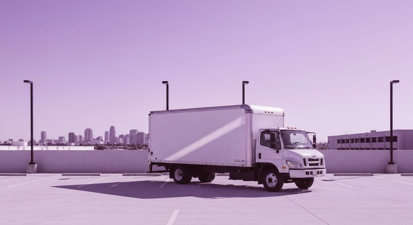 White moving truck parked in a modern urban lot with a soft purple city skyline in the background