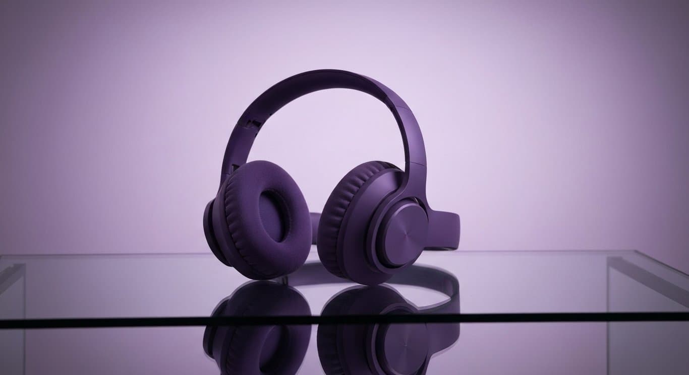 Headphones resting on a glass surface with a blurred purple background