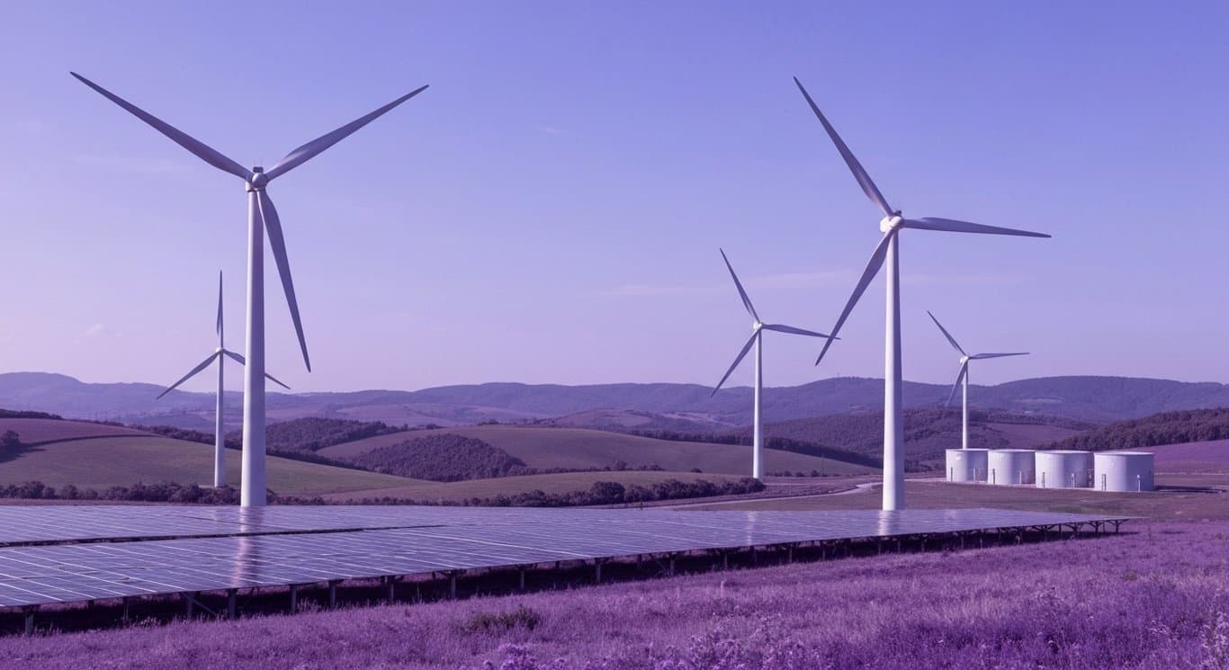 Wind turbines and solar panels stand among green hills with small battery units under a soft purple sky