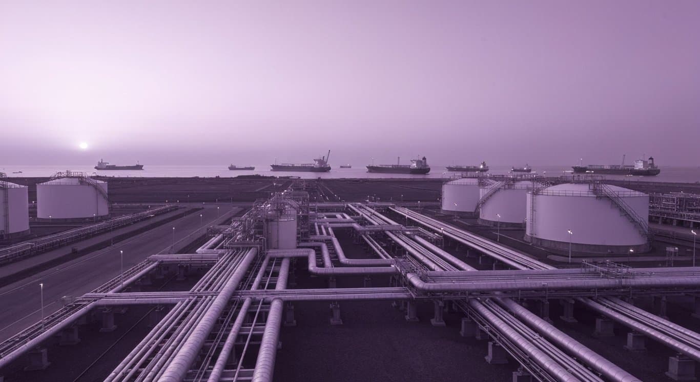 Liquefied natural gas facility with pipelines and tanks near a port at dusk
